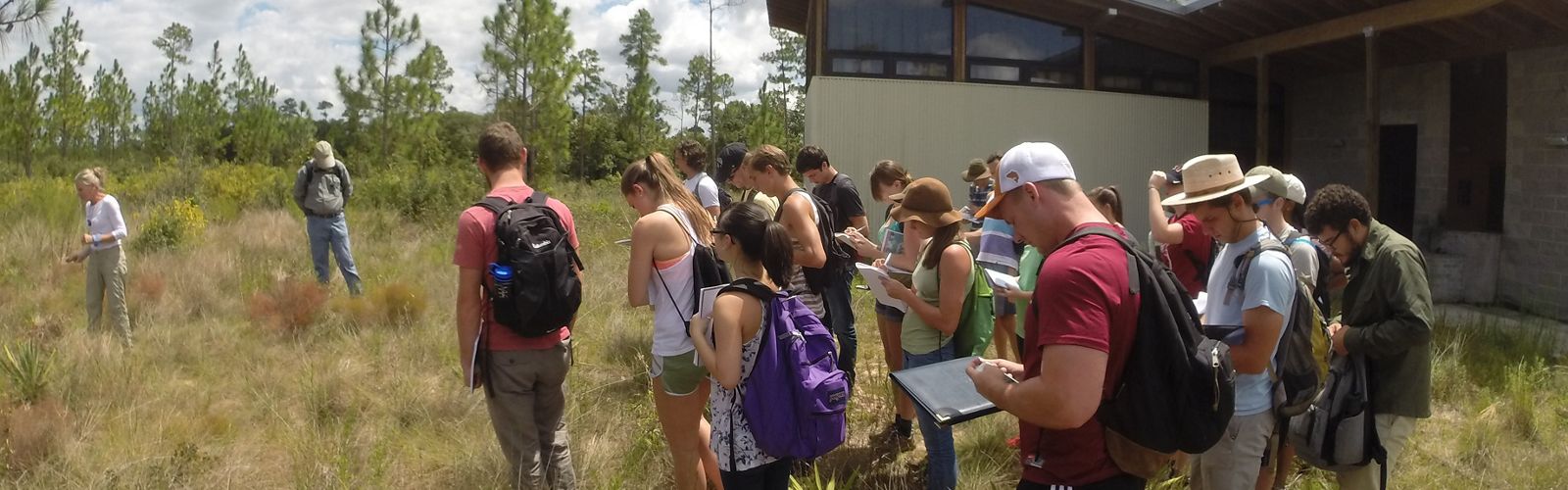 Students writing notes in an outdoor field setting.