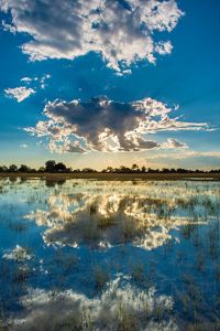 The sun behind a cloud reflected over water.