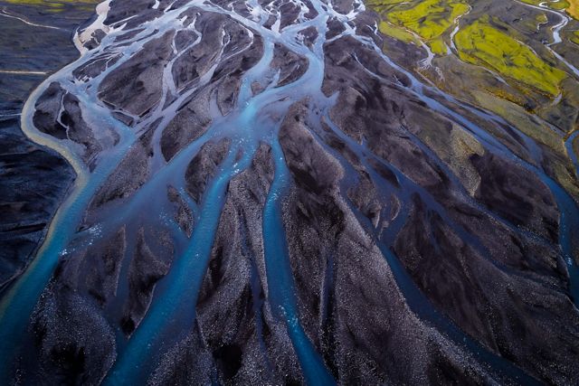 Aerial of several river channels weaving and crossing each other over black soil in Iceland